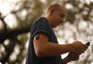 Eversense user examines a phone outdoors, with a medical CGM sensor attached to their upper arm.
